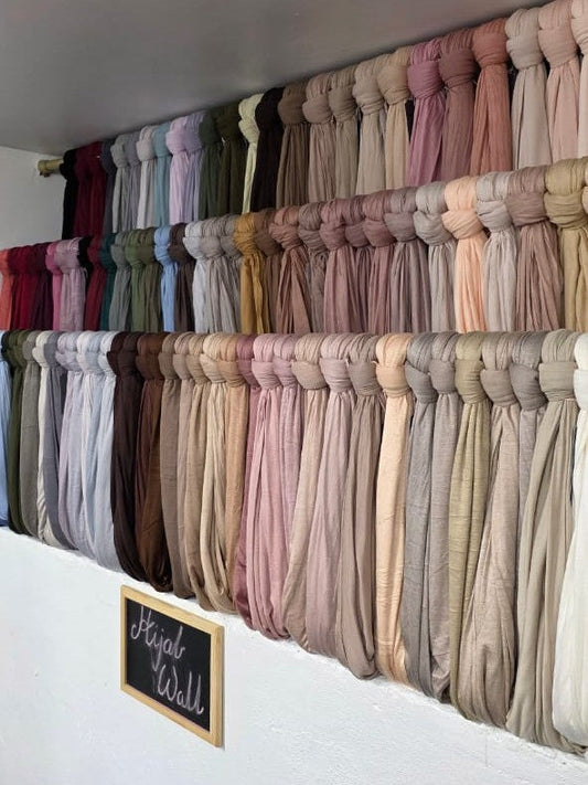 Wall display featuring a full range of hijabs in various colors and fabrics neatly arranged.