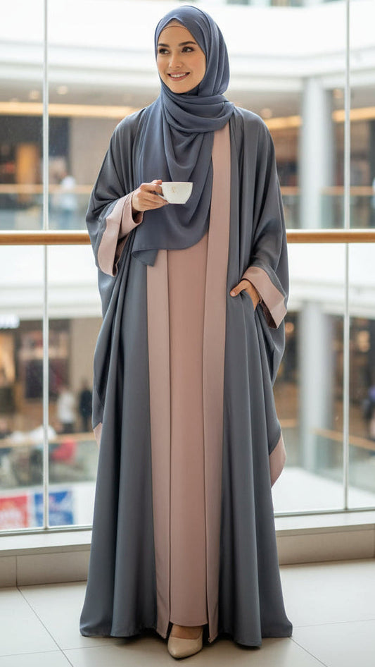 Woman in a gray abaya with a beige dress holding a cup in a modern indoor setting.
